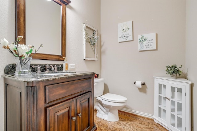 bathroom with baseboards, wood finished floors, vanity, and toilet