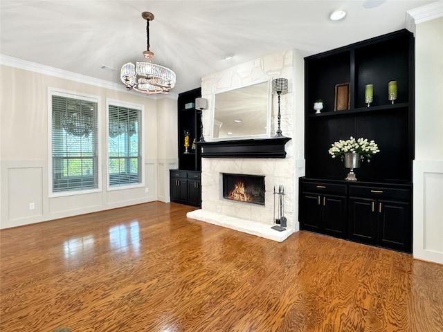 unfurnished living room featuring an inviting chandelier, wood finished floors, a decorative wall, crown molding, and a fireplace