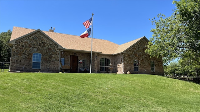 view of front facade with roof with shingles, stone siding, a chimney, and a front yard