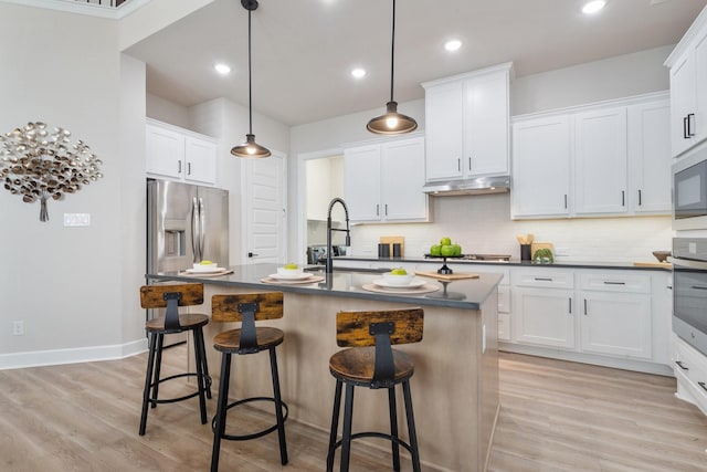kitchen with a sink, appliances with stainless steel finishes, dark countertops, light wood-type flooring, and an island with sink