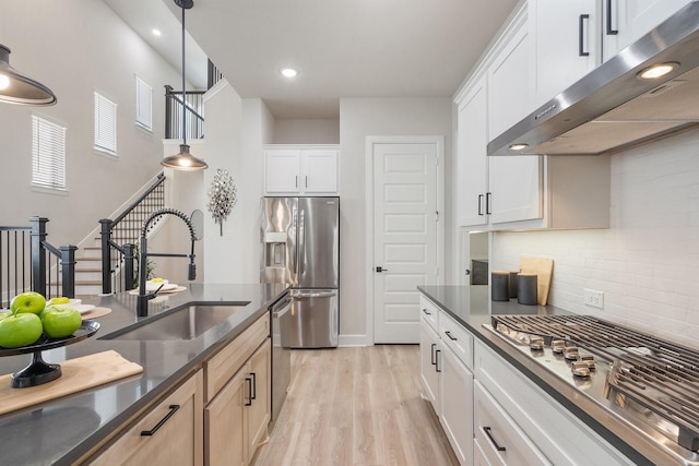 kitchen with a sink, under cabinet range hood, decorative backsplash, light wood-style flooring, and appliances with stainless steel finishes