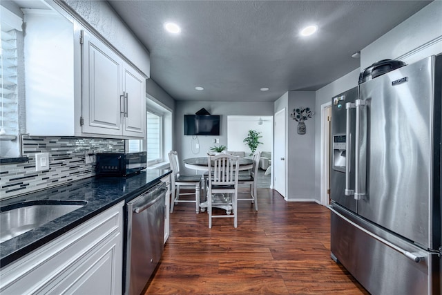 6110 Caracas Dr, Dallas, TX 75232 - kitchen featuring backsplash, dark stone counters, dark wood-style floors, white cabinets, and appliances with stainless steel finishes