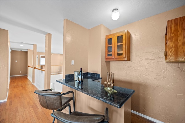 4730 Parkhaven Dr, Garland, TX 75043 - kitchen with a kitchen breakfast bar, hardwood / wood-style flooring, dark stone counters, glass insert cabinets, and brown cabinetry