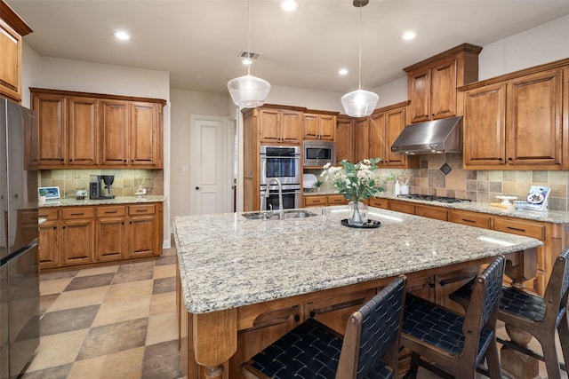 1715 San Jacinto Dr, Allen, TX 75013 - kitchen with under cabinet range hood, stainless steel appliances, a sink, a breakfast bar, and brown cabinets