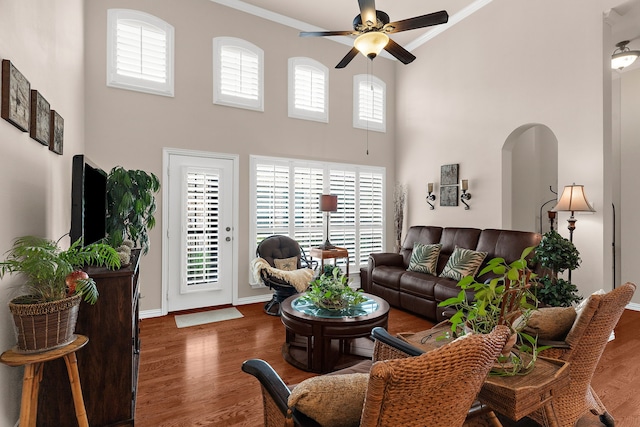 living area with a ceiling fan, a high ceiling, arched walkways, and ornamental molding
