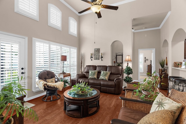 living room with ornamental molding, arched walkways, a ceiling fan, and a high ceiling