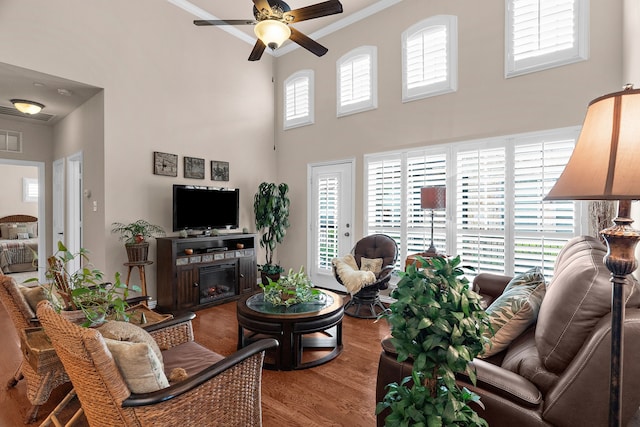 living area featuring a towering ceiling, a ceiling fan, wood finished floors, and ornamental molding