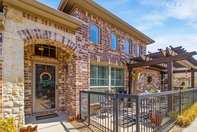 view of exterior entry featuring brick siding, stone siding, and a pergola