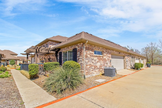 view of side of home featuring a pergola, a shingled roof, an attached garage, cooling unit, and brick siding