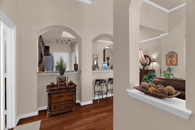 corridor with arched walkways, wood finished floors, crown molding, and baseboards