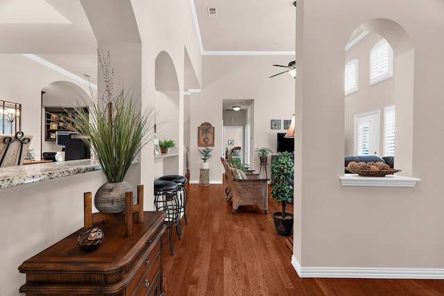 entryway with a ceiling fan, crown molding, wood finished floors, baseboards, and a high ceiling