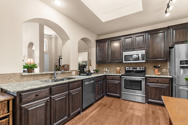 kitchen featuring a sink, light wood-style flooring, appliances with stainless steel finishes, and dark brown cabinetry