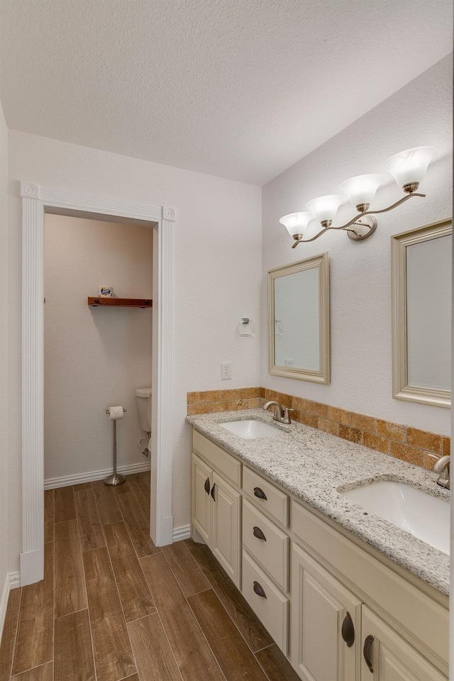 bathroom with a textured ceiling, double vanity, a sink, and wood finish floors