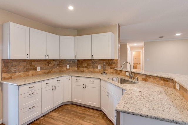 kitchen with a sink, backsplash, white cabinetry, and light stone counters