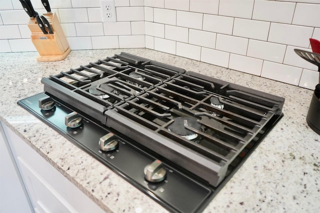 interior details featuring light stone counters, backsplash, and black gas stovetop