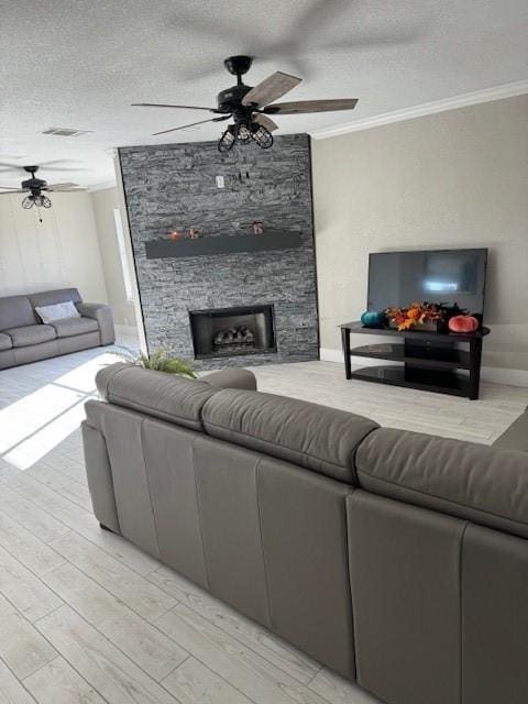 living room featuring a textured ceiling, ceiling fan, crown molding, and a stone fireplace