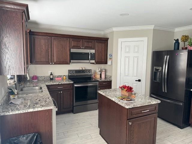 kitchen with light wood finished floors, ornamental molding, a kitchen island, appliances with stainless steel finishes, and a sink