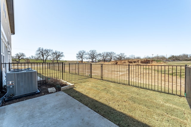 view of yard with a fenced backyard, central air condition unit, a rural view, and a patio