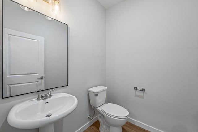 half bath featuring toilet, a sink, baseboards, and wood finished floors