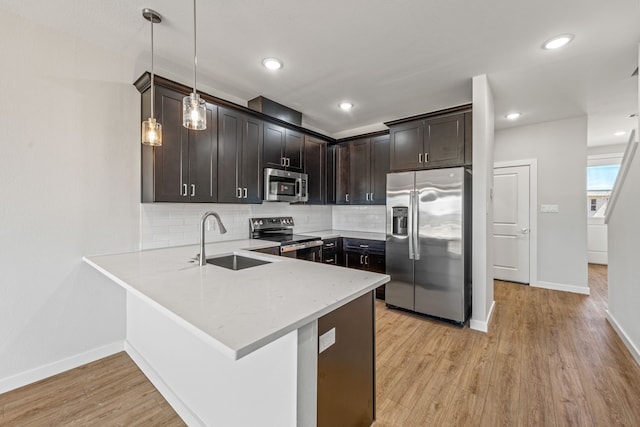 kitchen with a sink, appliances with stainless steel finishes, a peninsula, light wood-type flooring, and dark brown cabinets