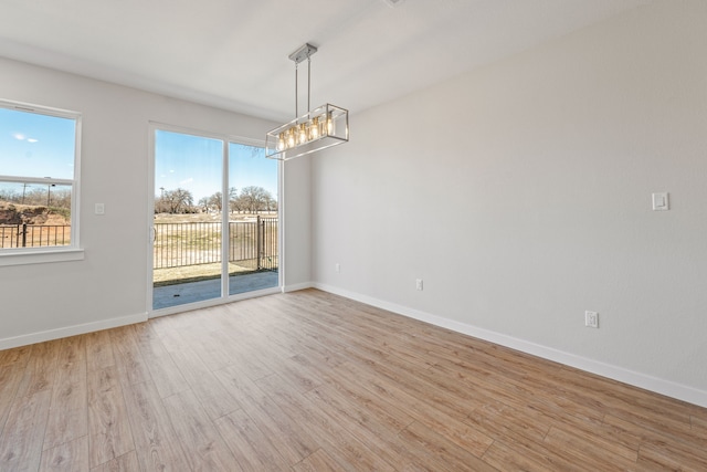 empty room featuring a wealth of natural light, a notable chandelier, baseboards, and wood finished floors