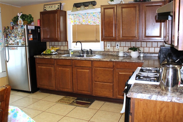 1090 N Race St, Stephenville, TX 76401 - kitchen with under cabinet range hood, decorative backsplash, a sink, light tile patterned flooring, and freestanding refrigerator