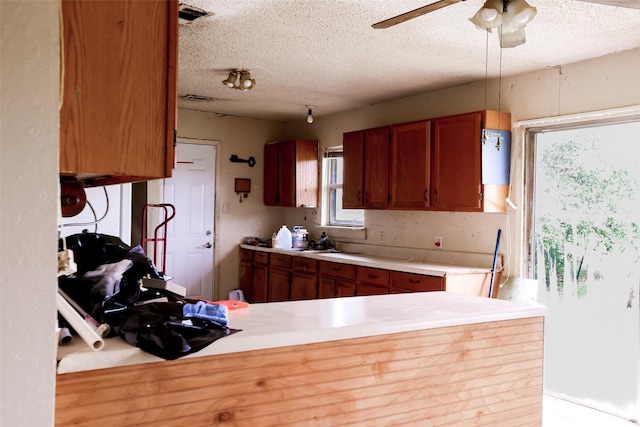 kitchen with brown cabinetry, a sink, a textured ceiling, and light countertops