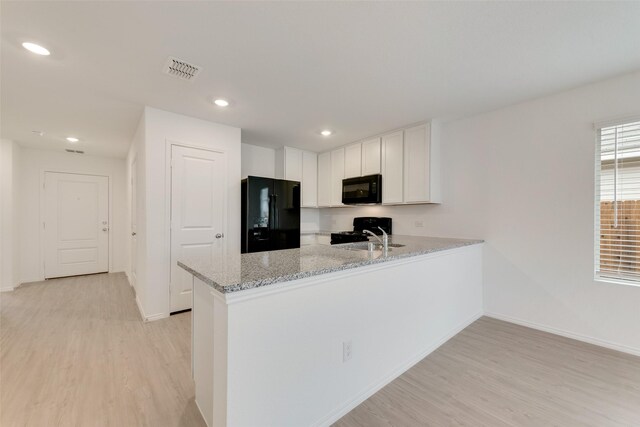 kitchen featuring a peninsula, light wood finished floors, visible vents, light stone countertops, and black appliances
