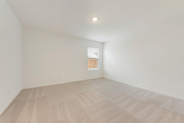 spare room featuring light colored carpet and baseboards