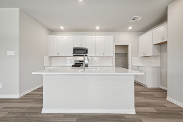 kitchen featuring wood finished floors, a center island with sink, appliances with stainless steel finishes, white cabinetry, and a sink