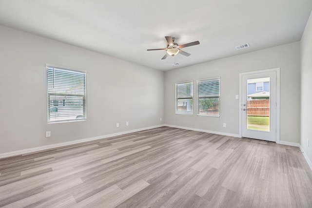 empty room with light wood-type flooring, a ceiling fan, baseboards, and visible vents