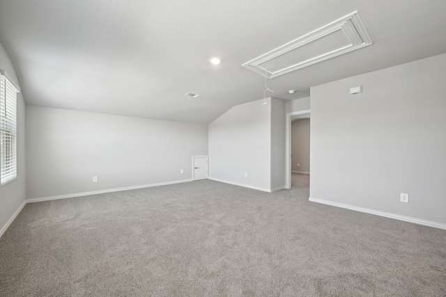 carpeted empty room with baseboards, attic access, and vaulted ceiling