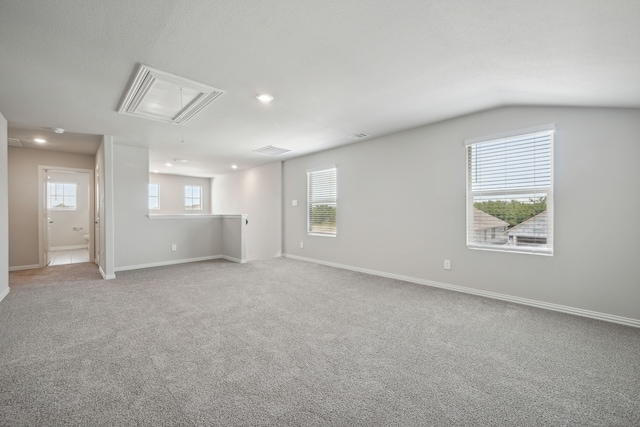 empty room featuring attic access, a wealth of natural light, visible vents, and light carpet