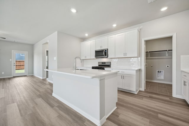 kitchen with recessed lighting, decorative backsplash, a center island with sink, a sink, and appliances with stainless steel finishes