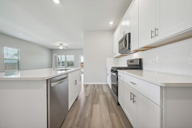 kitchen featuring light countertops, stainless steel appliances, an island with sink, a sink, and backsplash