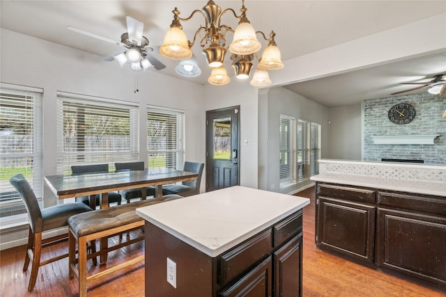 kitchen featuring decorative light fixtures, light wood-type flooring, a center island, ceiling fan with notable chandelier, and dark brown cabinets