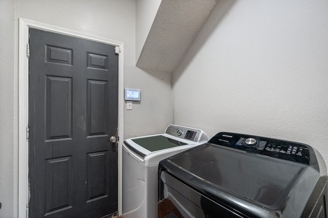 clothes washing area featuring a textured wall, washer and dryer, and laundry area