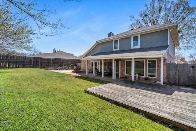 rear view of property with brick siding, a chimney, a fenced backyard, and a yard