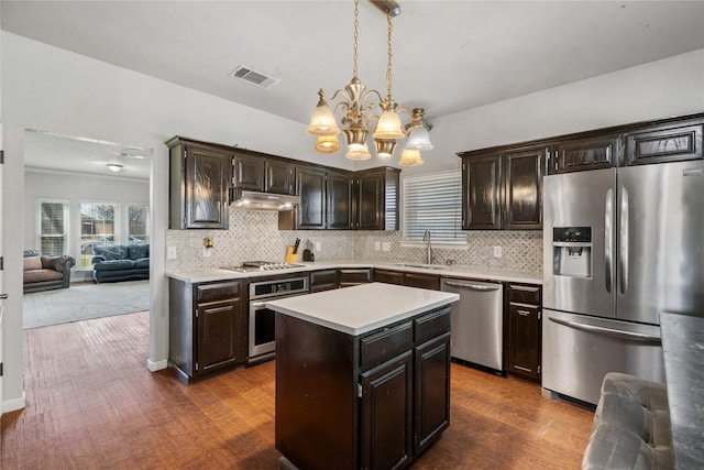 kitchen featuring an inviting chandelier, stainless steel appliances, under cabinet range hood, a sink, and visible vents