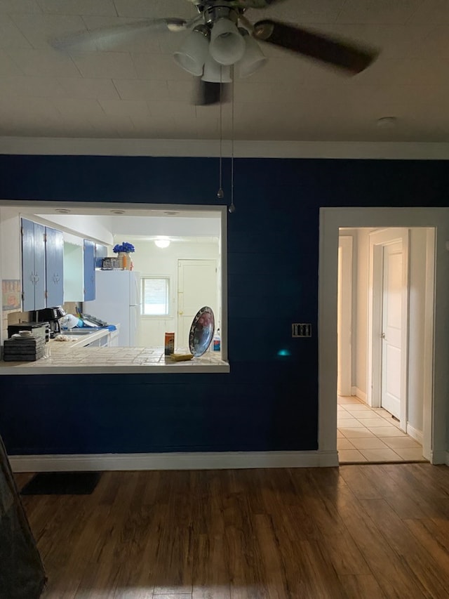 kitchen with light countertops, freestanding refrigerator, wood finished floors, baseboards, and ceiling fan