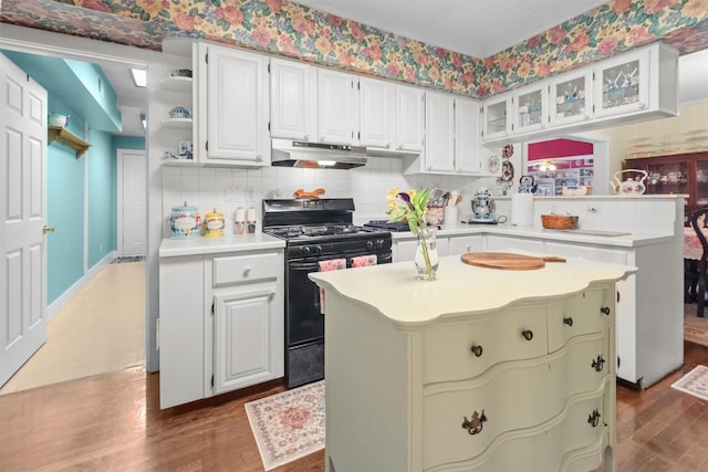 kitchen featuring dark wood-style flooring, glass insert cabinets, light countertops, under cabinet range hood, and black gas range
