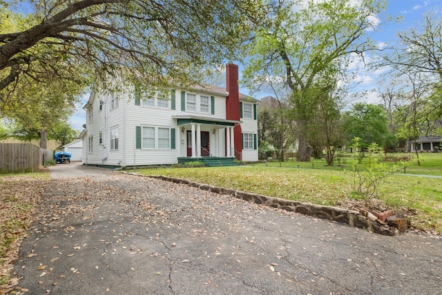 view of front of house featuring driveway, a chimney, fence, and a front lawn