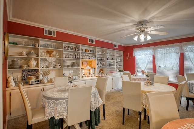 carpeted dining space with visible vents, crown molding, and a ceiling fan