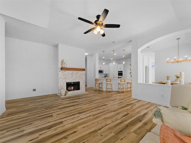 4512 Stepping Stone Dr, Fort Worth, TX 76123 - living area featuring ceiling fan with notable chandelier, baseboards, arched walkways, light wood finished floors, and a tile fireplace