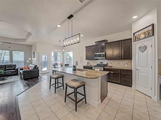 kitchen featuring tasteful backsplash, appliances with stainless steel finishes, a sink, open floor plan, and a kitchen breakfast bar