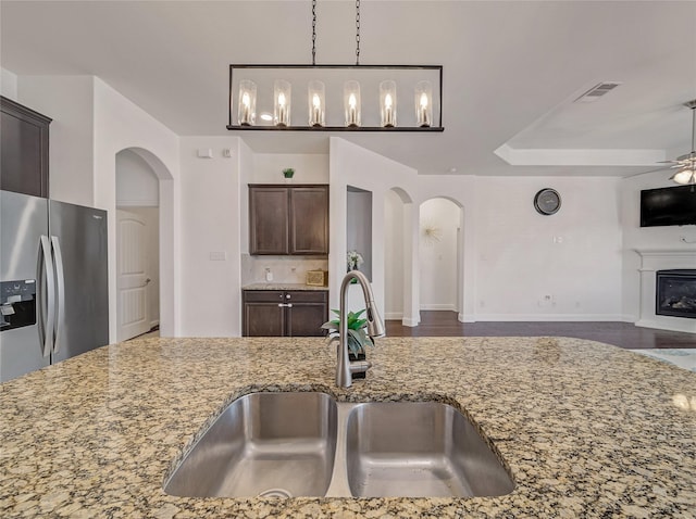 kitchen with visible vents, light stone countertops, arched walkways, a sink, and stainless steel fridge with ice dispenser