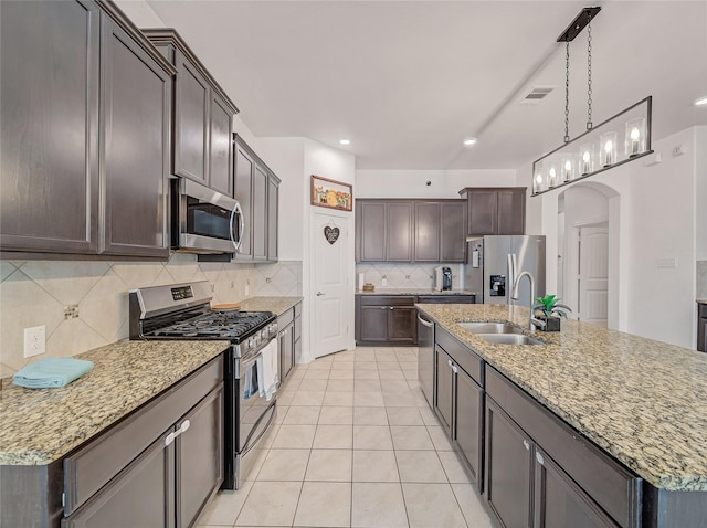 kitchen with tasteful backsplash, a sink, arched walkways, a kitchen island with sink, and appliances with stainless steel finishes
