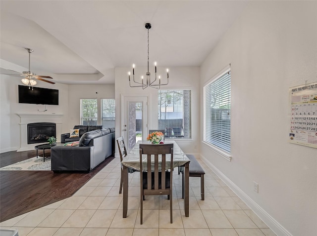 dining area with light tile patterned flooring, a tray ceiling, baseboards, and a glass covered fireplace
