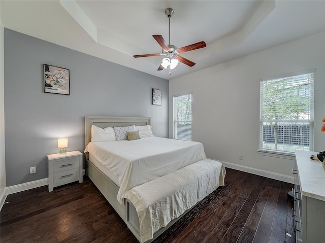 bedroom featuring baseboards, dark wood-style floors, a tray ceiling, and ceiling fan
