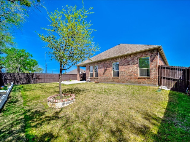 back of house with a lawn, brick siding, a fenced backyard, and roof with shingles